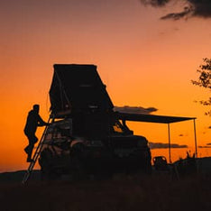 A sunset scene with a man climbing into a TentBox Cargo roof tent