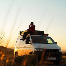 A man sitting on his Volkswagen Transporter with a TentBox Lite installed on the roof