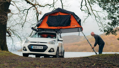 Person setting up TentBox Lite 1.0 roof tent near lake