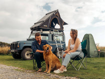 A couple sitting in front of their TentBox Cargo which is mounted on a Landrover Defender