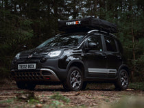 A closed TentBox Lite 2.0 roof tent installed onto a black Fiat car in the woods